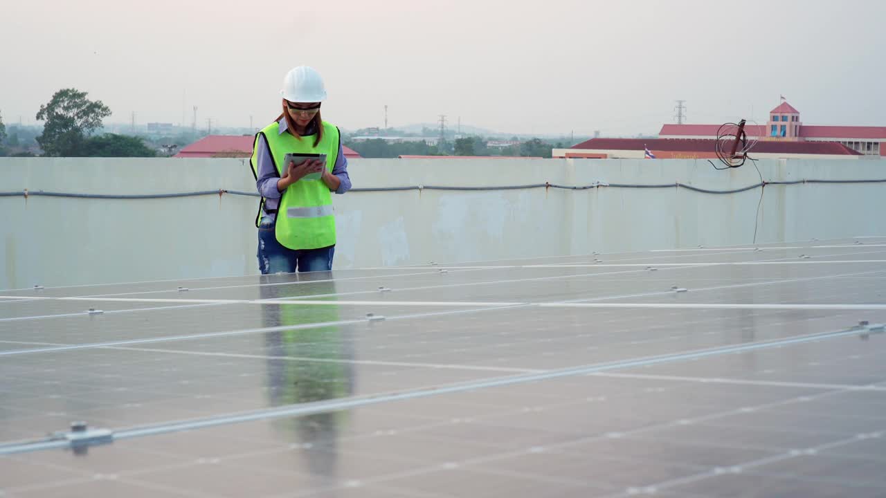 身穿制服的亚洲女工程师，在太阳能电池板厂使用平板电脑视频素材