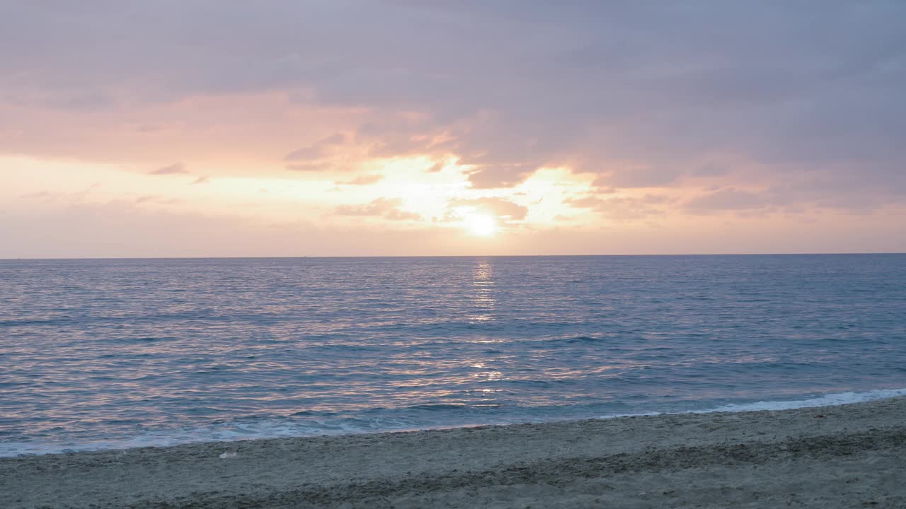 美丽的日落与多云的橙色天空在海上。太阳触及海平面。海浪溅起浪花，产生白色泡沫，冲击着沙滩。热带海景视频素材