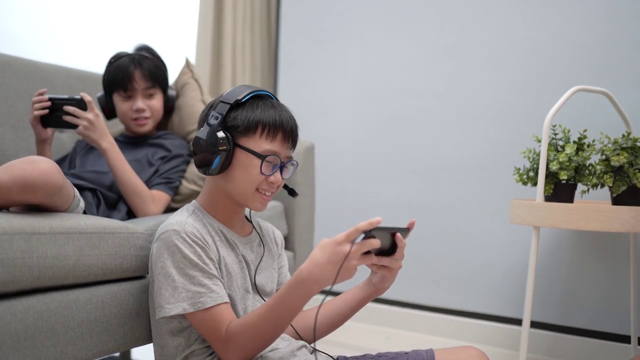 两个亚裔华人兄弟坐在客厅的沙发上玩电子游戏视频下载