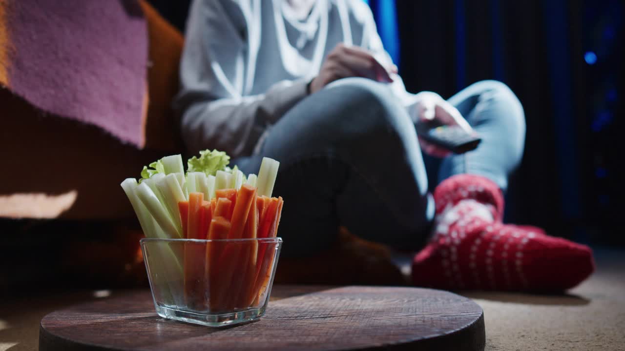 女人坐在地上，一边看电视一边吃芹菜和胡萝卜条视频下载