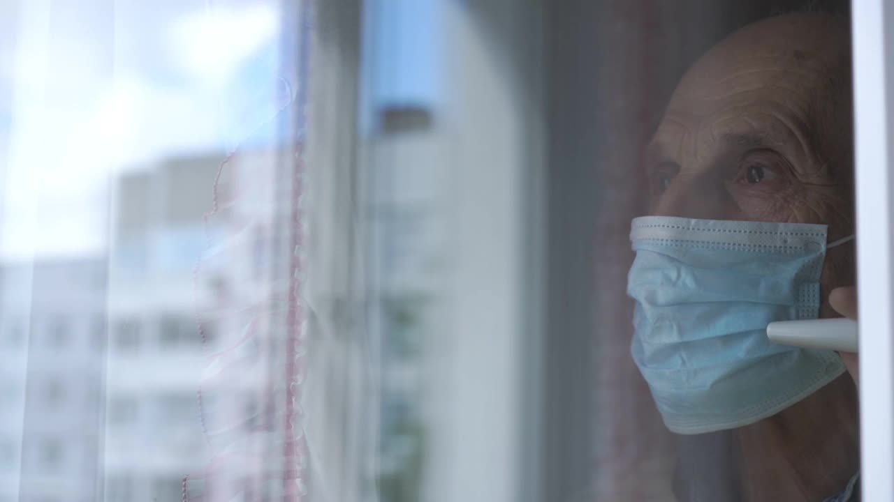 戴面具的老人站在窗户前，窗户上有建筑物的倒影视频素材