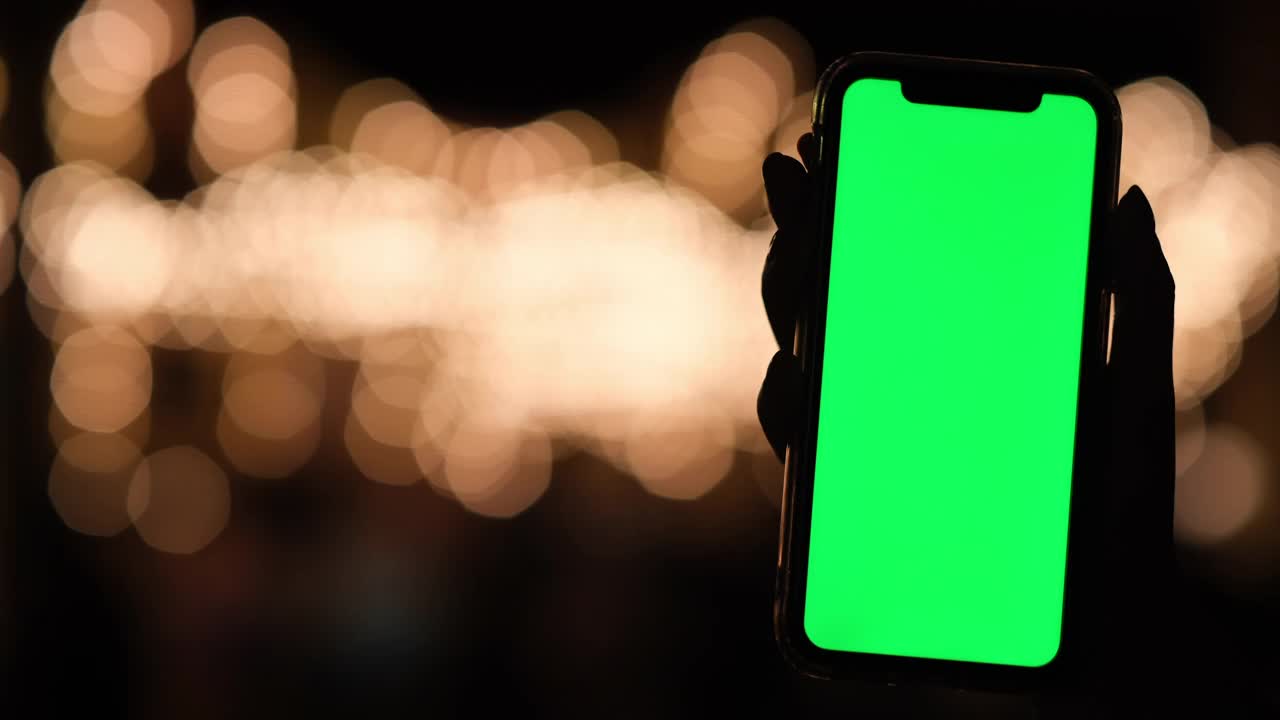 手握绿色屏幕的智能手机在晚上。金色的焦外成像背景视频素材