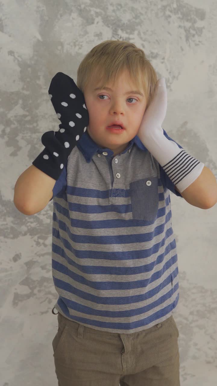 可爱的唐氏综合症小男孩，手上拿着袜子玩捉迷藏。垂直格式视频素材