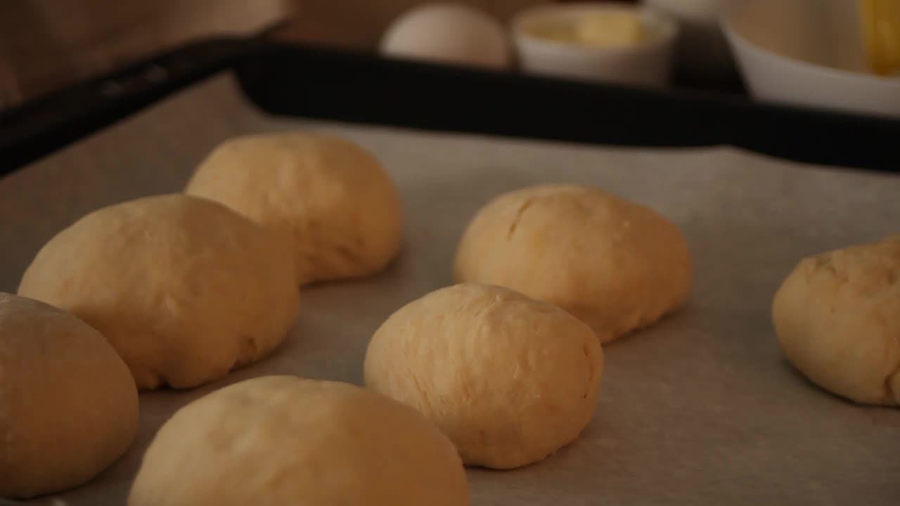 新鲜的自制全麦芝麻汉堡面包。女人在烘烤之前先用手给面团抹油视频素材