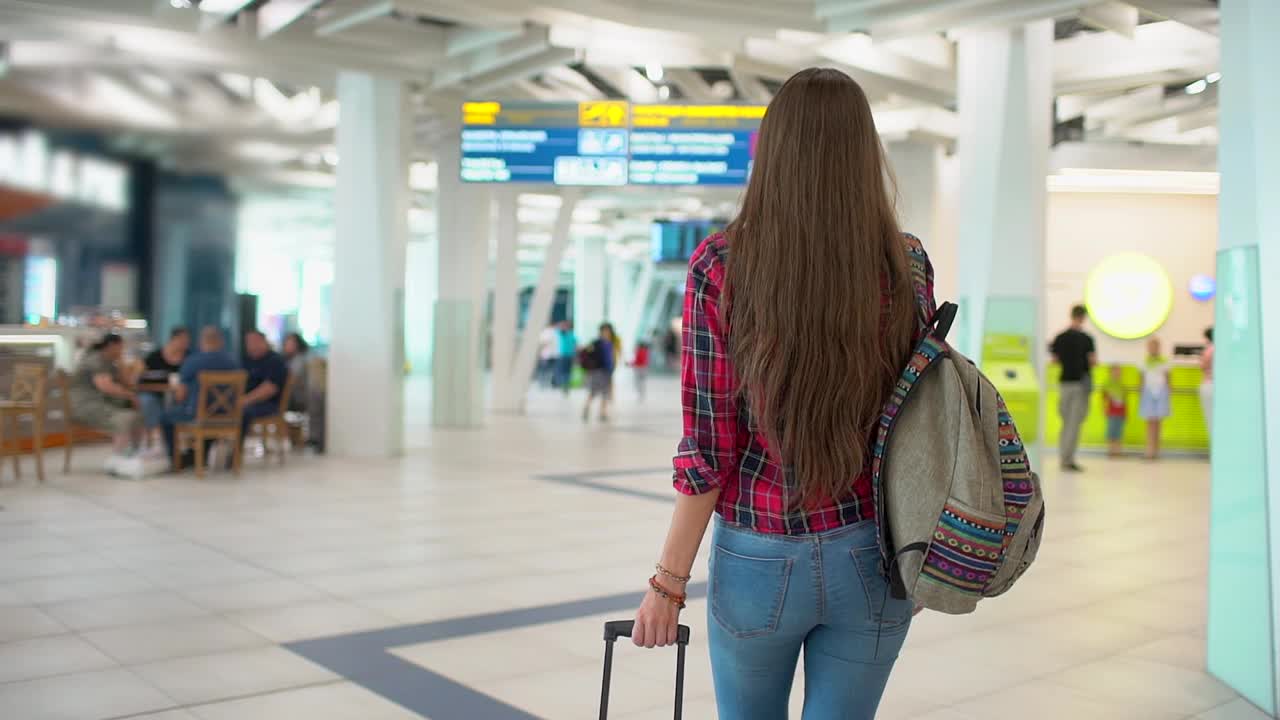 年轻的女旅客穿着休闲衬衫和行李走在现代化的机场航站楼视频素材