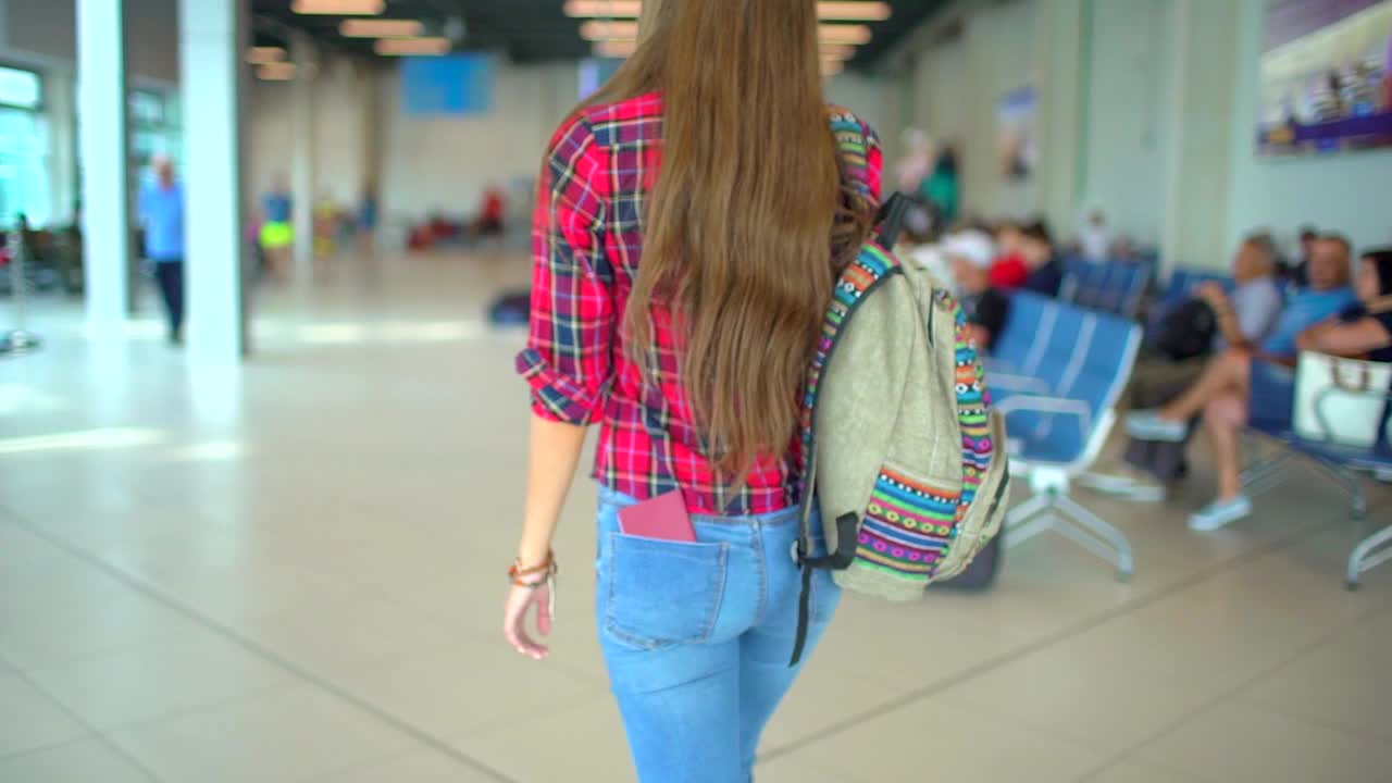 年轻的女游客，女游客穿着休闲衬衫，带着行李走在机场候机厅，从后面看视频素材