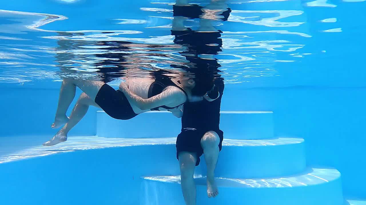 水下的亚洲华人男子拉着并帮助妻子浮在游泳池上，放松练习呼吸练习为他们的新生儿做准备视频下载