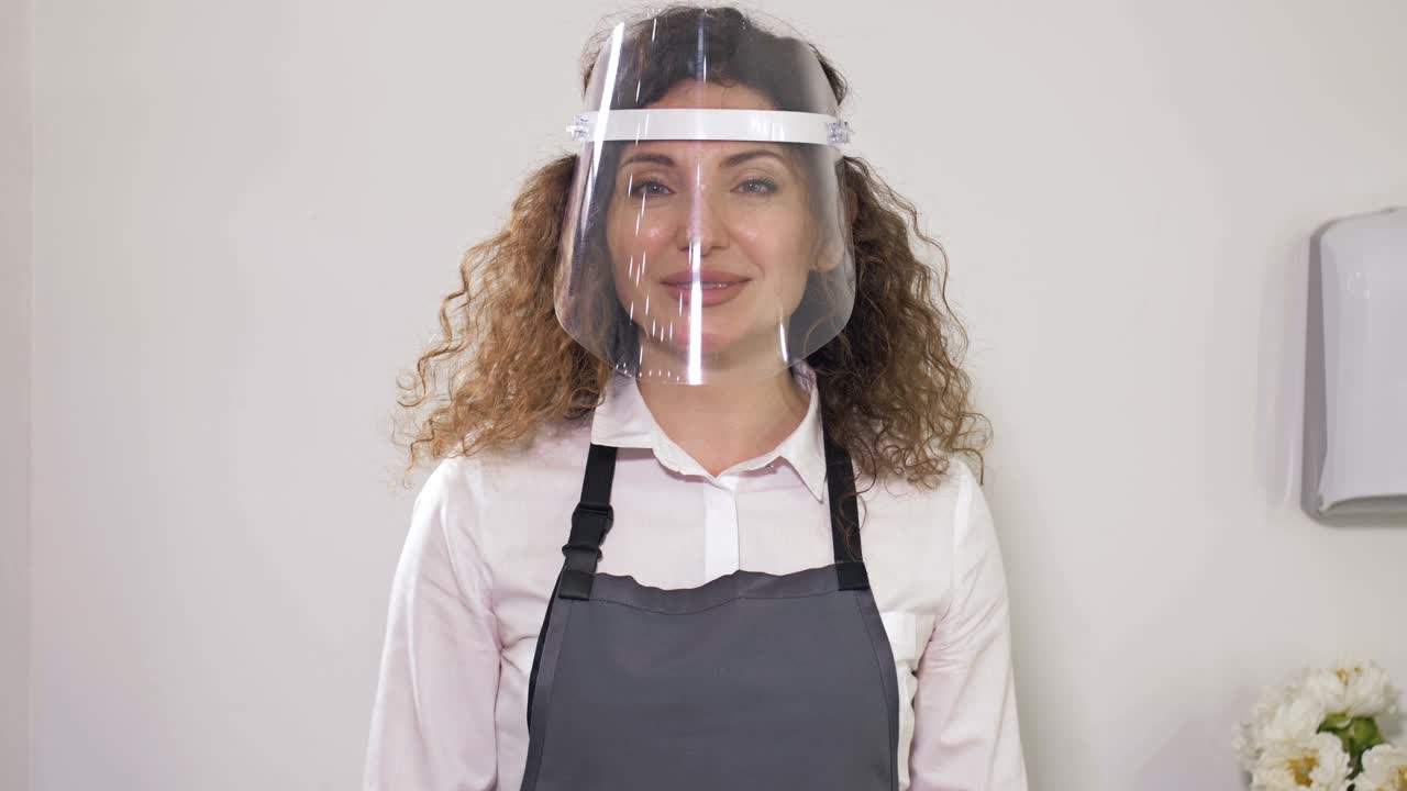 一个女售货员在一个咖啡馆戴着塑料防护面具的肖像。冠状病毒大流行期间的交易规则视频下载