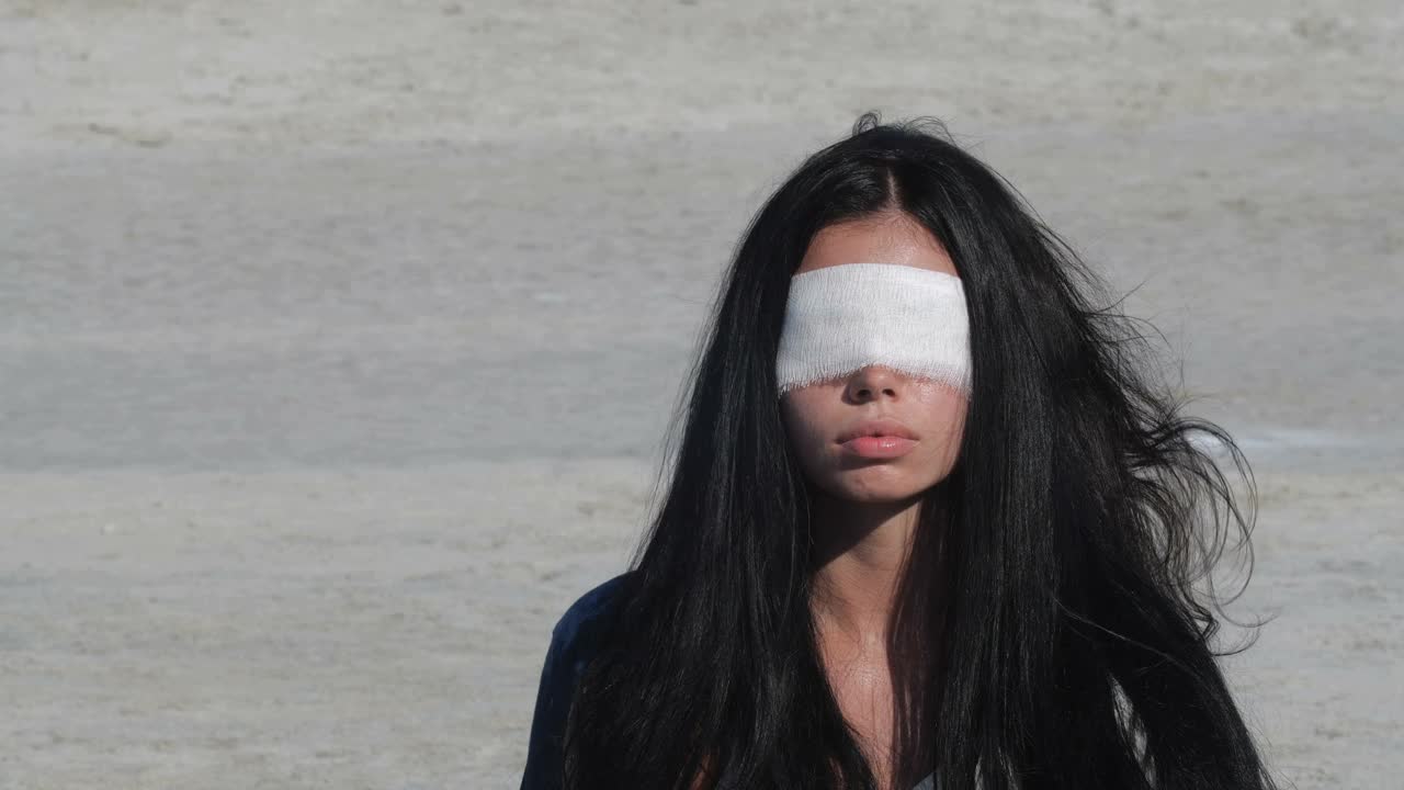 一个女人的近距离肖像蒙着眼睛和长长的黑发。绷带上有血迹。户外沙漠拍摄。4K fps慢动作视频下载
