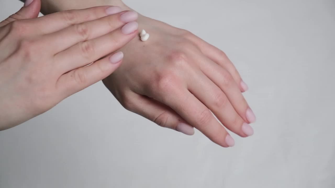 一名女子用润肤霜涂抹手部干燥的皮肤在白色的背景上。视频下载