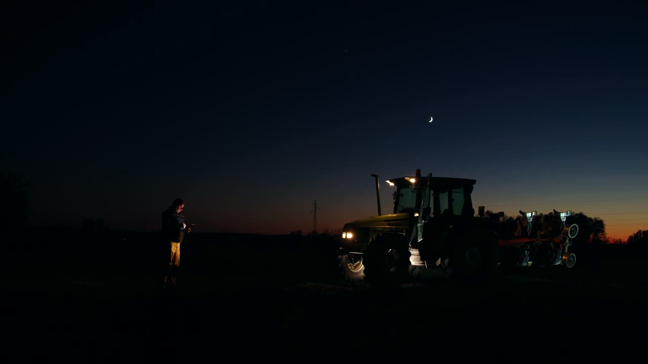 晚上在拖拉机旁使用智能手机的农民视频素材