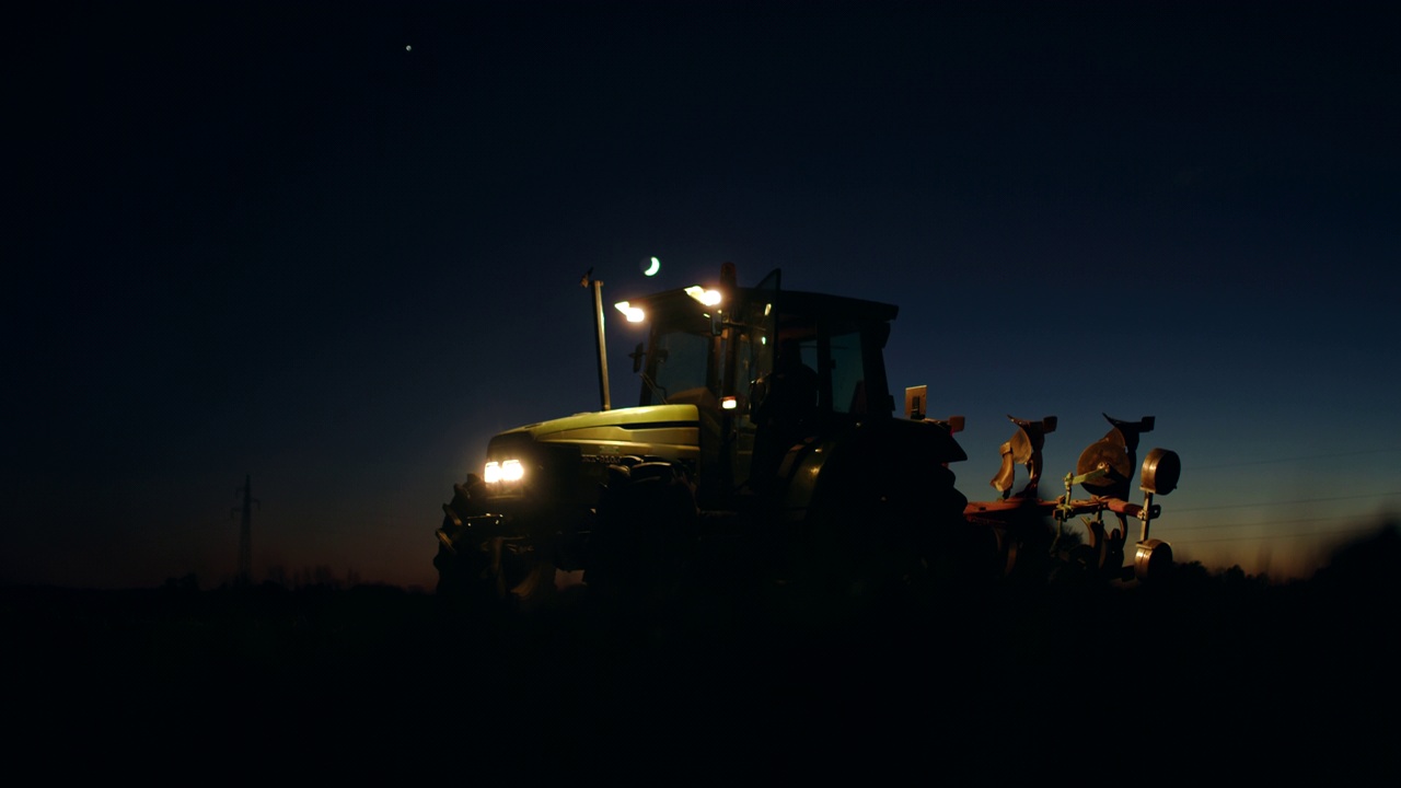 一个无法辨认的农民在晚上把他的拖拉机留在田里视频素材