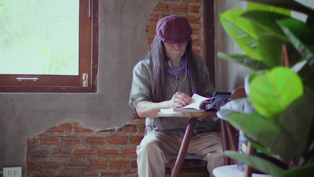 肖像的亚洲高级男子听音乐与耳机和拍照与智能手机坐在咖啡厅咖啡厅，高级男子工作的移动设备，人们的生活方式技术概念视频下载