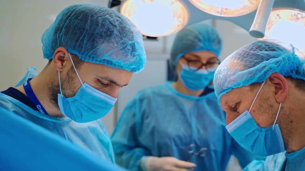 两名男性专家和助手正在做手术。身穿蓝色制服的专业外科医生在手术中使用医疗器械。视频素材