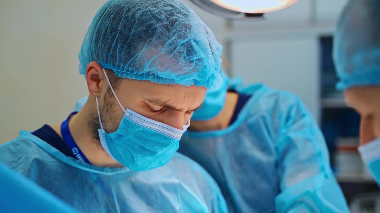 戴着蓝色面具向下看的医生的肖像。经验丰富的外科医生在手术室里挽救病人的生命。特写镜头。视频素材