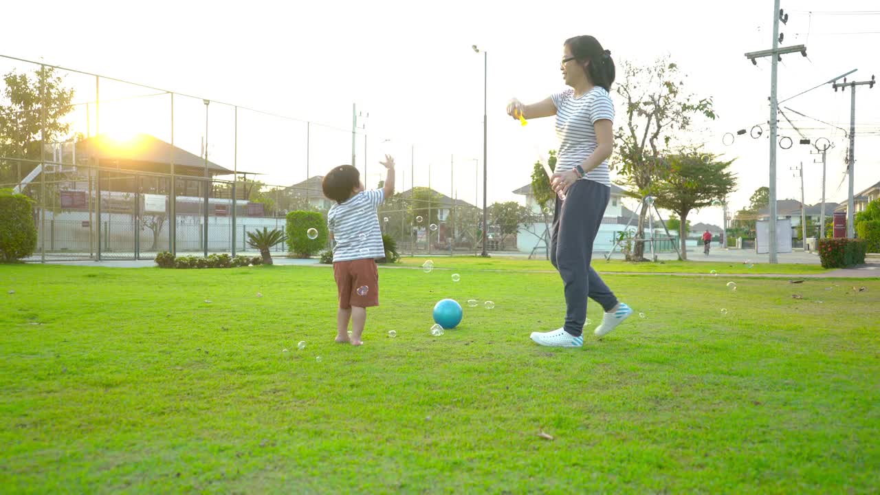快乐的亚洲小男孩和他的妈妈一起在操场上玩肥皂泡视频下载