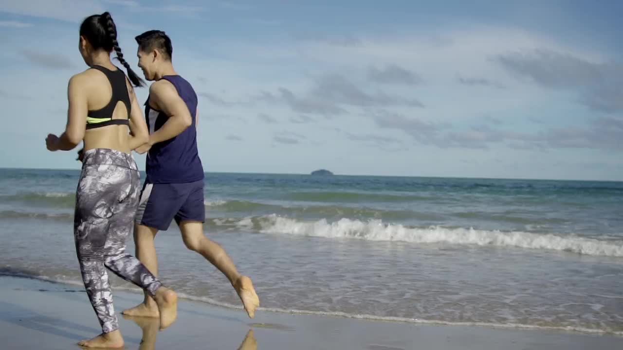 一对年轻的亚洲夫妇在海滩上跑步或慢跑的镜头。视频素材