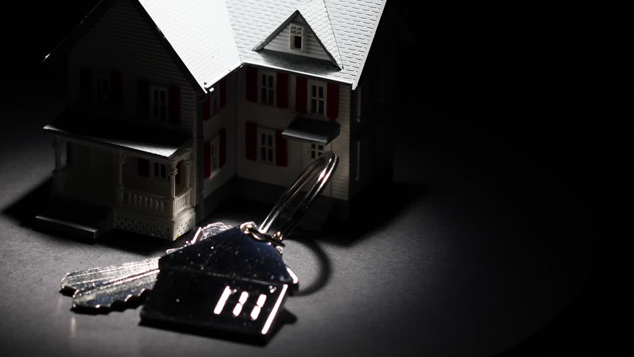 聚光灯模型家和钥匙上的房子钥匙链缓慢旋转在黑暗的背景视频下载