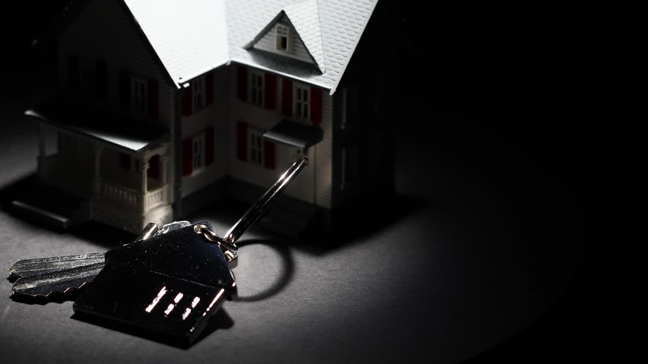 聚光灯模型家和钥匙上的房子钥匙链缓慢旋转在黑暗的背景视频下载