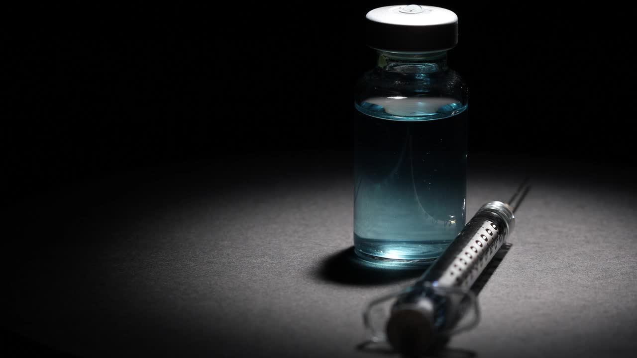 聚光灯下医用疫苗瓶和注射器在黑色表面和黑色背景上旋转视频下载