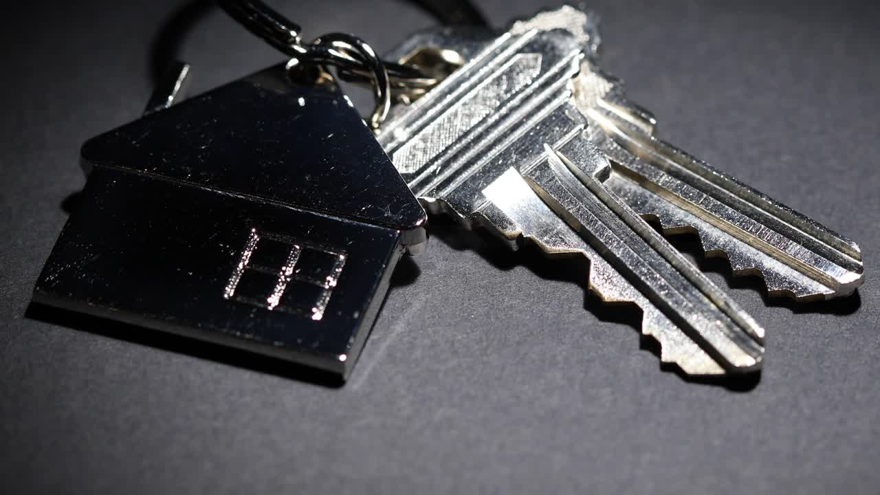 聚光灯钥匙和房子钥匙链缓慢旋转在黑暗的背景视频下载