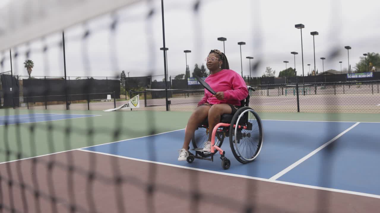 年轻的黑人残疾妇女在轮椅上与朋友玩皮球视频素材