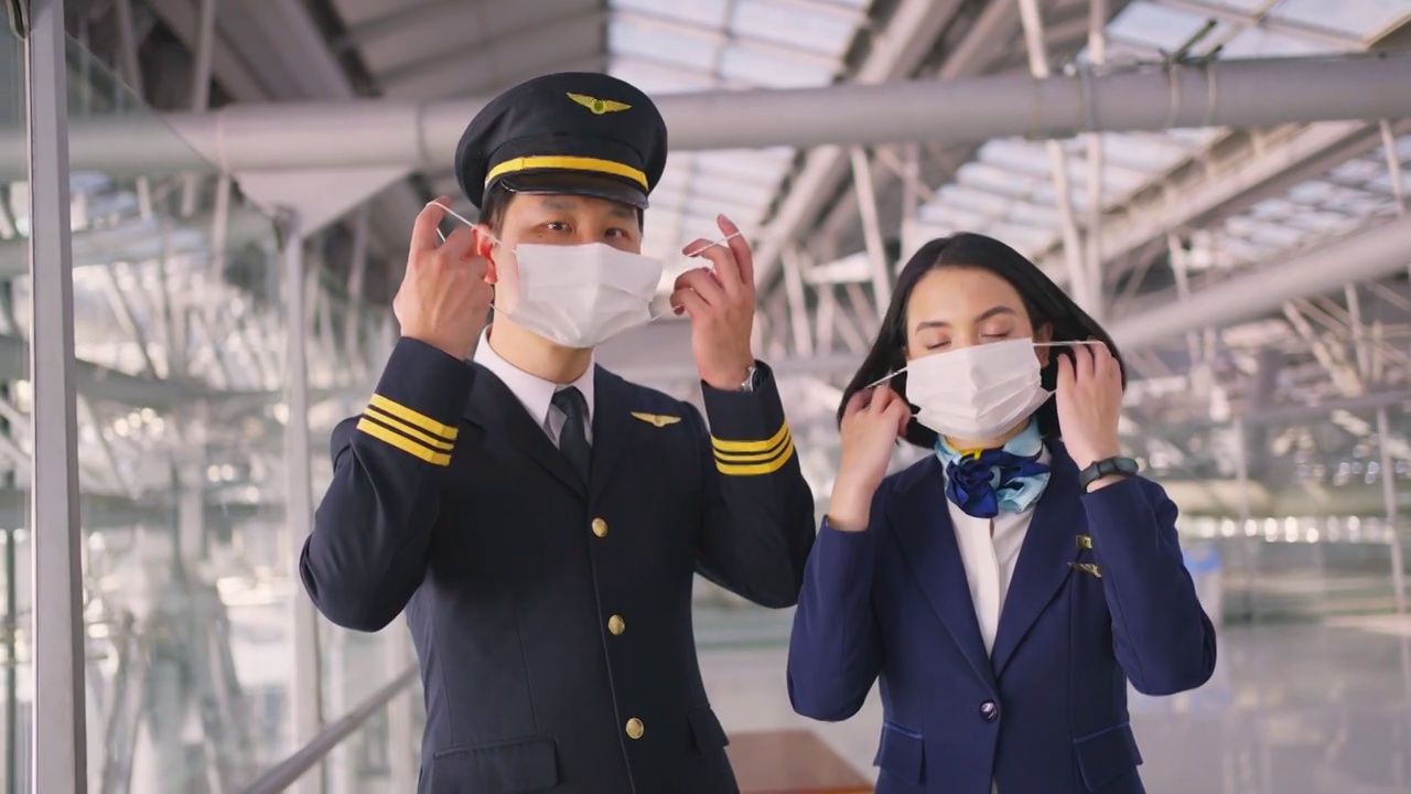 新冠肺炎疫情期间，飞行员和空乘人员戴口罩走在机场航站楼走向飞机，以预防新冠肺炎感染。航空运输的新常态生活理念。视频下载