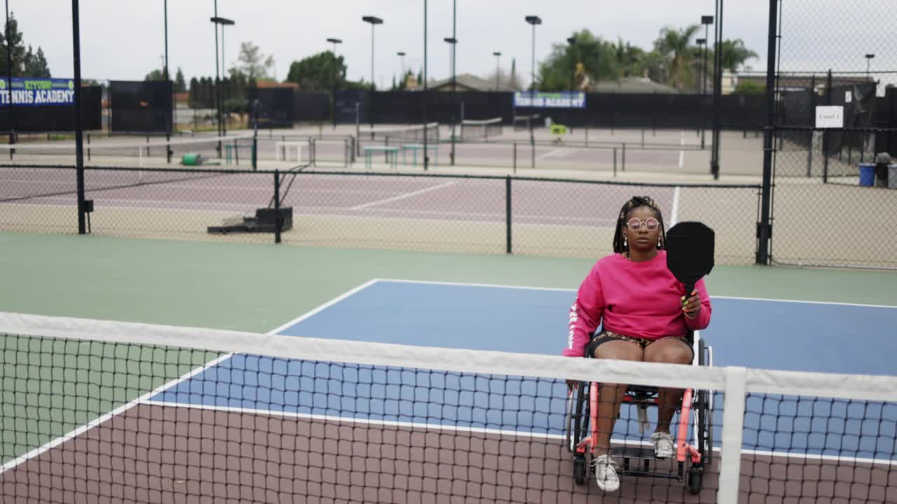 年轻的黑人残疾妇女在轮椅上与朋友玩皮球视频下载