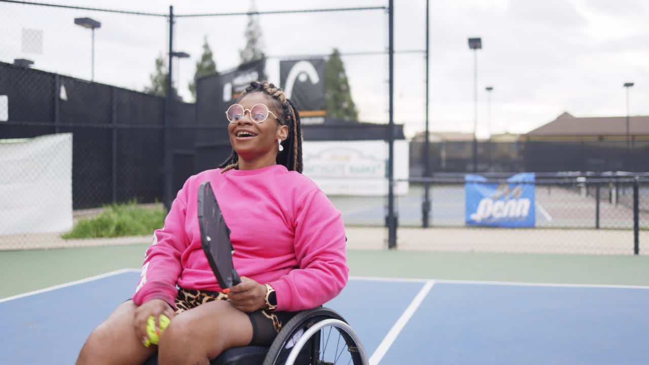 年轻的黑人残疾妇女在轮椅上与朋友玩皮球视频素材