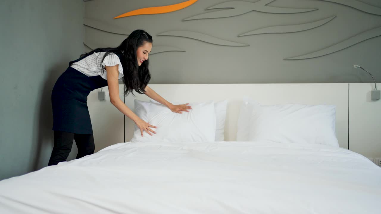 一个年轻的女仆带着医用口罩在酒店房间的床上更换床单。视频素材