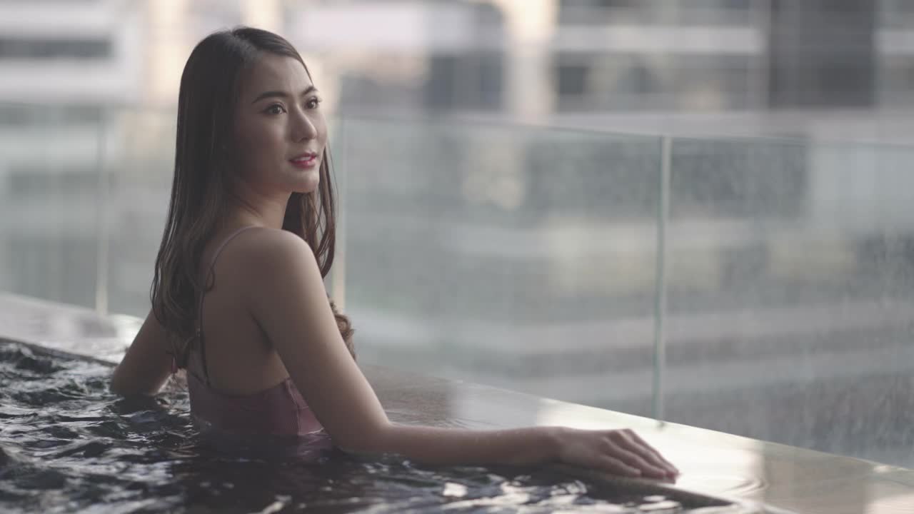 在一个漫长的暑假期间，亚洲妇女在游泳池游泳，在城市的背景。视频下载