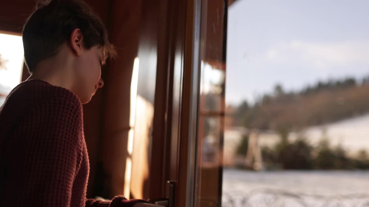小男孩打开了露台的滑动门，享受着阳光和冬天的新鲜空气。视频素材