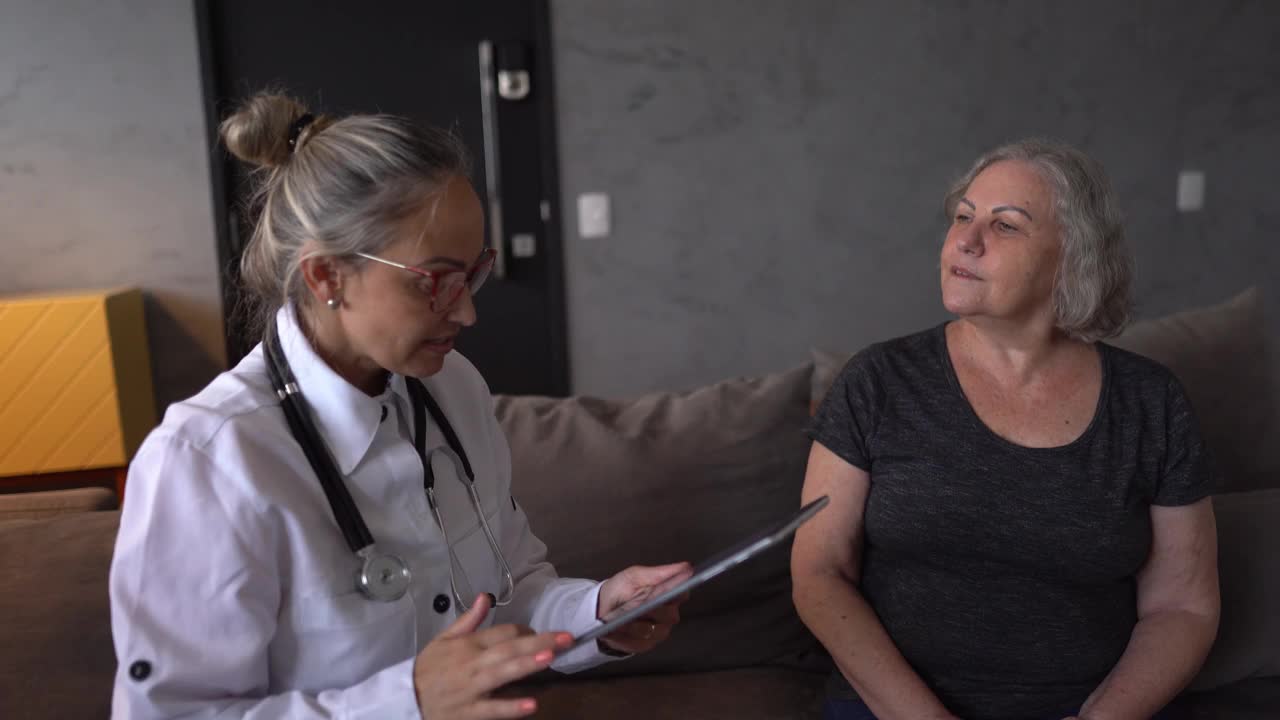 医生在家访中使用数字平板电脑与老年患者交谈视频下载