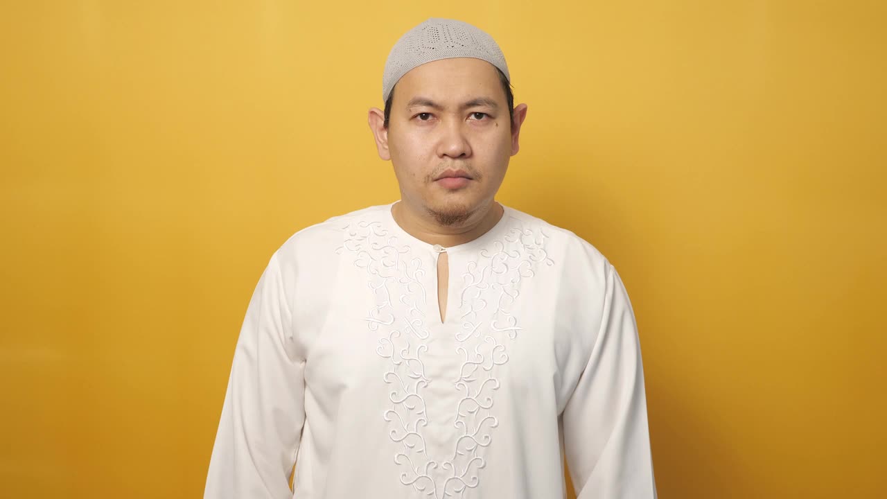 亚洲穆斯林男子做了嘘的手势，把手指放在嘴唇上，背对着黄色的背景偷偷讲八卦的概念视频素材