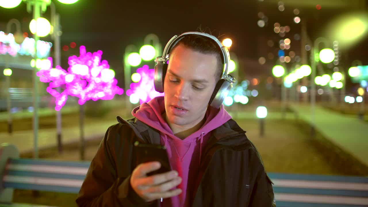 一个年轻人在街上戴着耳机。科技、互联网、通讯和人的概念——年轻人用智能手机和耳机听音乐视频素材