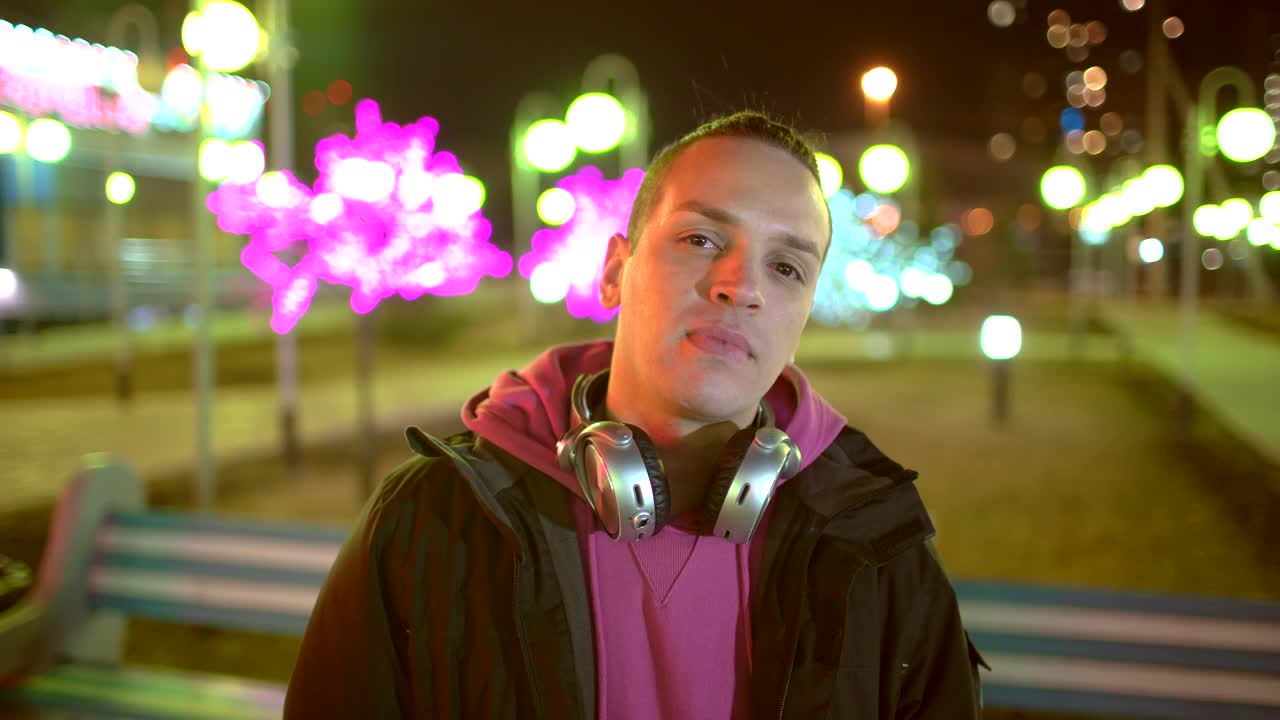 一名英俊的年轻人戴着黑色无线耳机听着智能手机里的音乐，在黄昏或傍晚的时候在欧洲老城中心的街道上跳舞视频素材