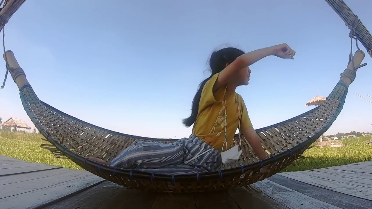 亚洲女孩躺在秋千吊床上，背景是天然稻田。视频素材