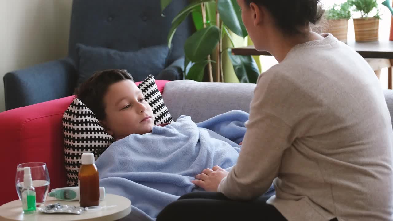 生病的男孩躺在家里的沙发上。他和他的母亲在一起视频下载