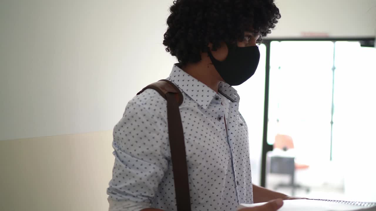 学生戴着口罩走在走廊上，使用笔记本视频素材