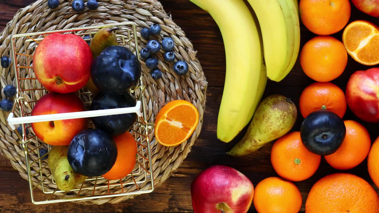 新鲜的水果在一个金色的购物篮中旋转，旁边的木质背景是大量的水果。价格上涨或鼓励购买健康食品的概念视频素材