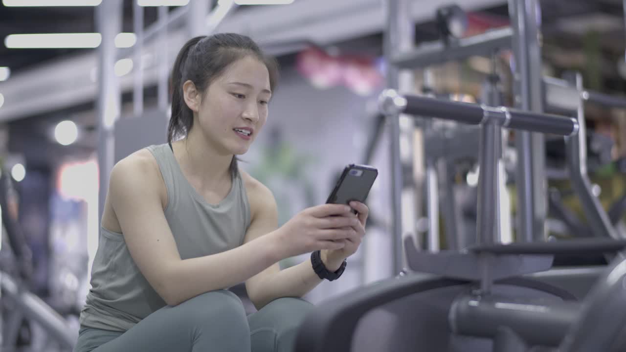 年轻的亚洲女性在健身房使用手机视频下载