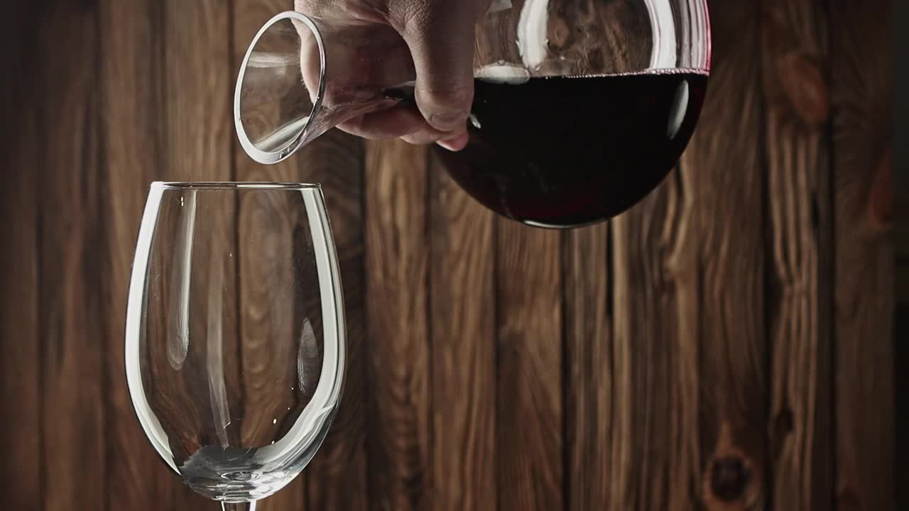 红酒慢慢地从醒酒器倒入葡萄酒杯中，背景是古老的木材视频素材