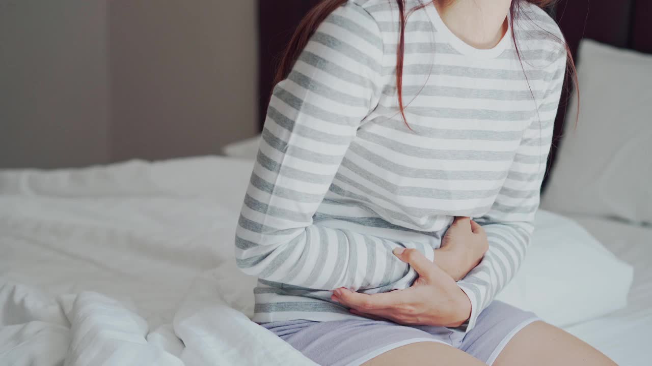 年轻女子胃痛，躺在床上。周期抽筋问题概念视频素材