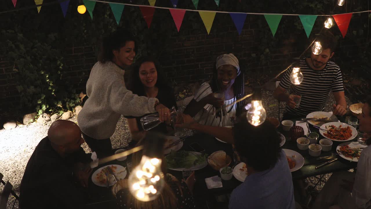 在后院的晚宴上，快乐的年轻女子为朋友斟酒视频素材