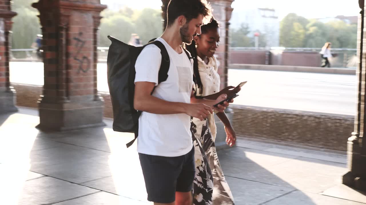 手持拍摄的年轻的多民族男女游客在城市行走时通过手机讨论视频素材