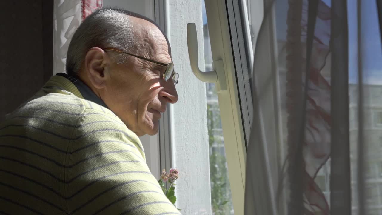 一位戴眼镜的老人站在窗前欣赏城市风景视频下载