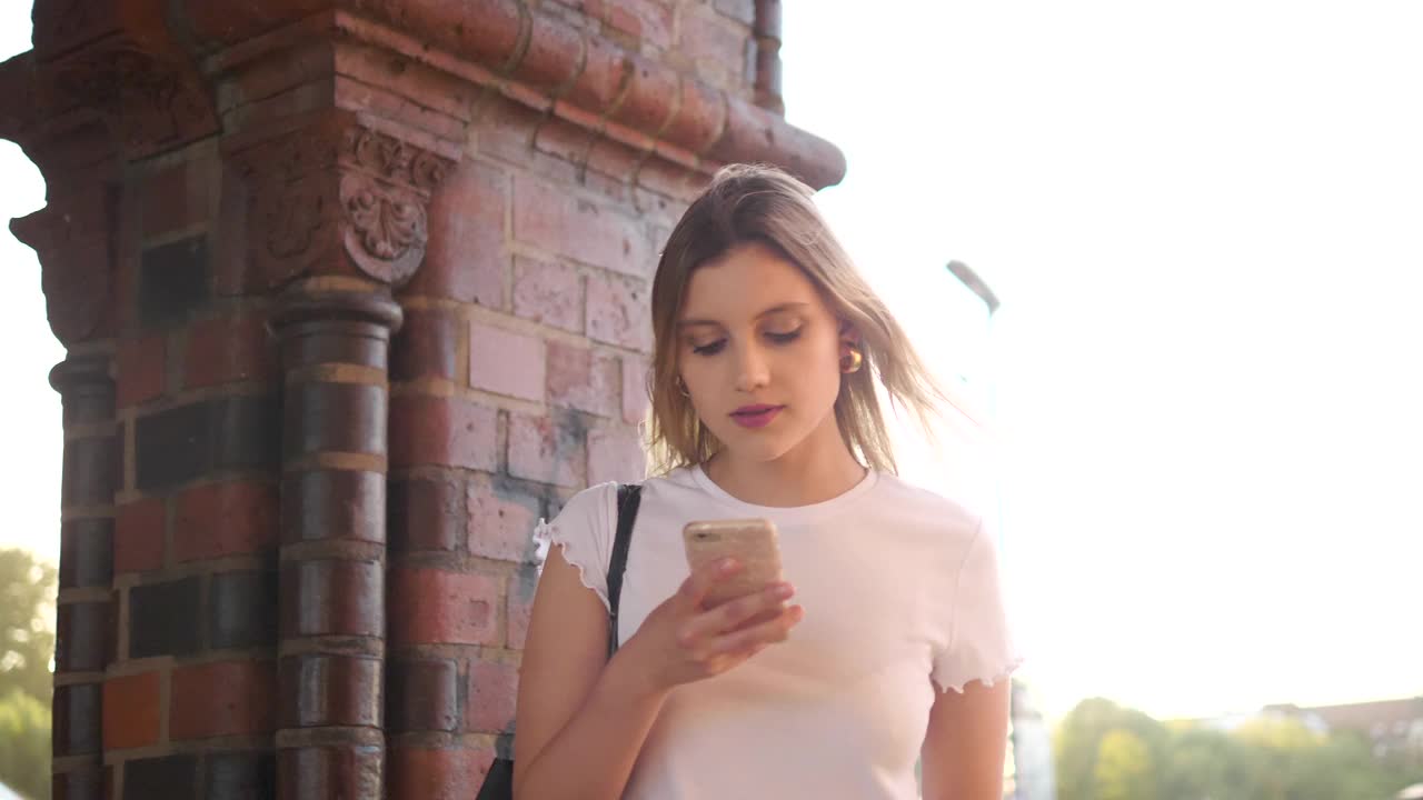 微笑的年轻女性游客通过智能手机发送短信，而行走在城市的人行道上视频素材