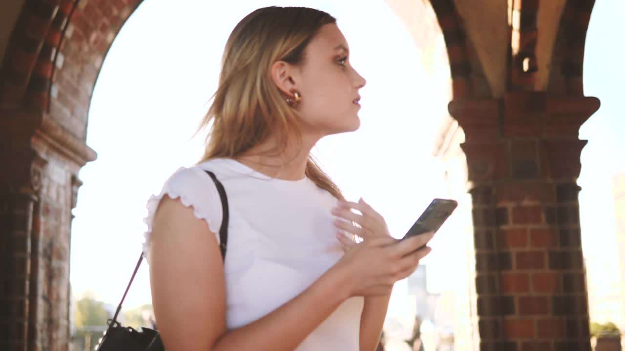 年轻的女游客拿着智能手机在城市里看别的地方视频素材