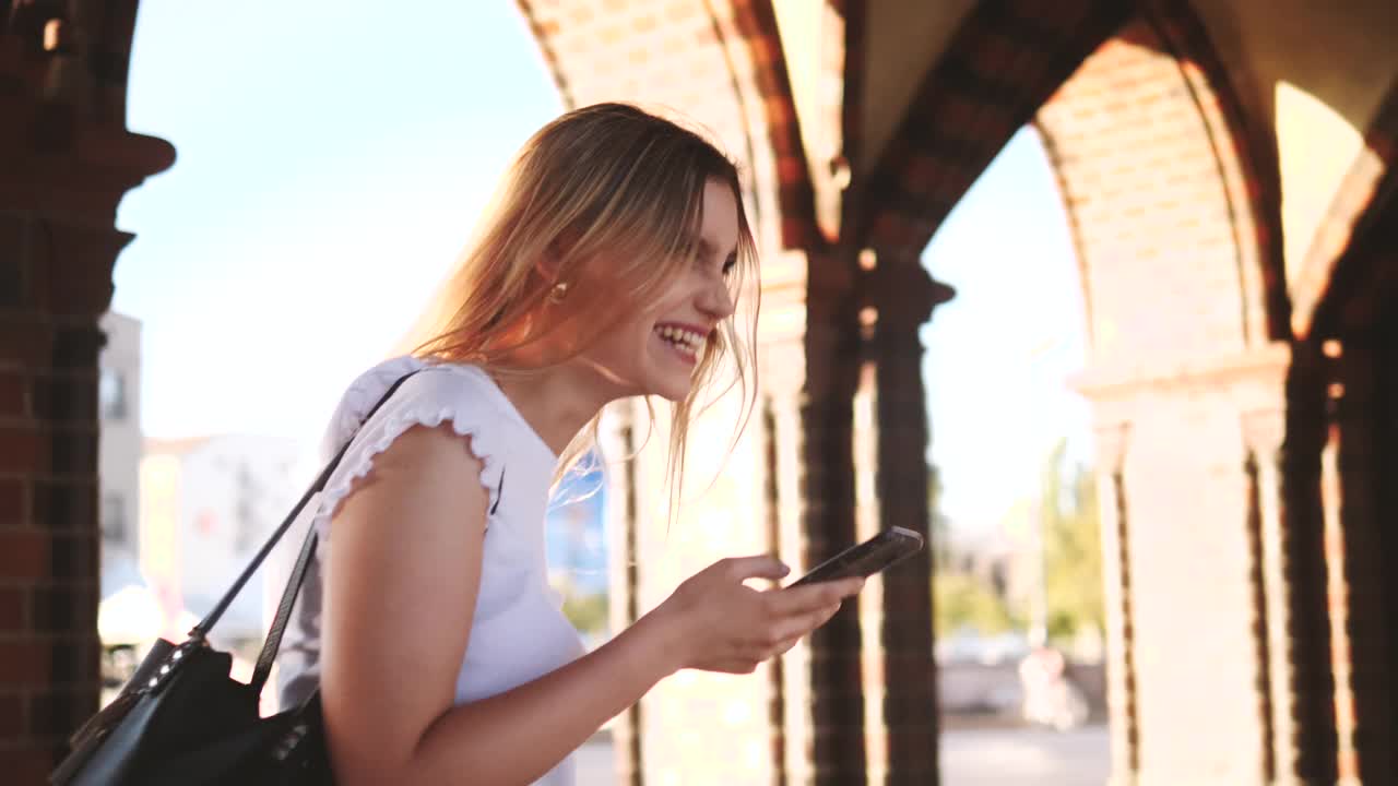 一个快乐的年轻女子在城市里用智能手机看短信视频素材
