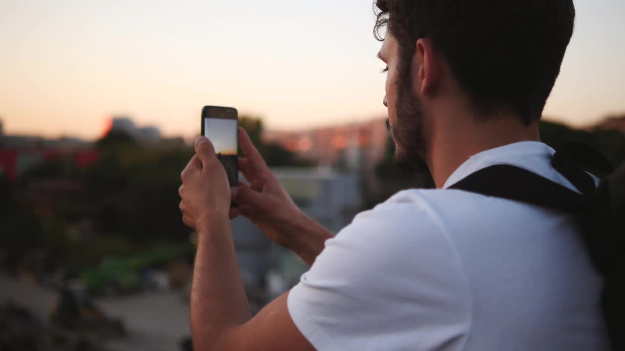 一个年轻人站在天桥上拍摄夕阳下的城市视频素材